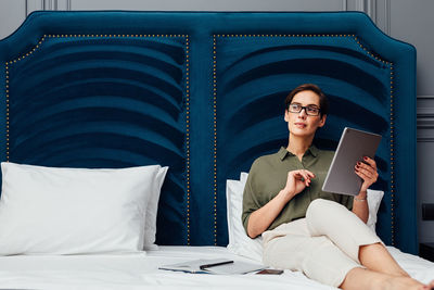 Businesswoman using digital tablet while sitting on bed