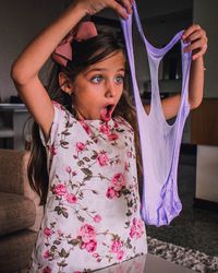 Shocked girl with mouth open looking at torn fabric while standing in house