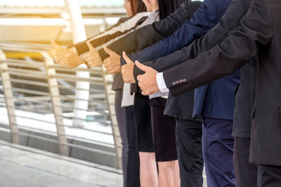 Midsection of businesspeople gesturing thumbs up sign