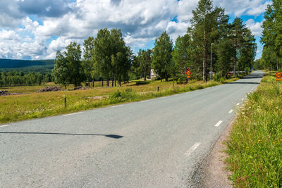 Road by trees in city against sky