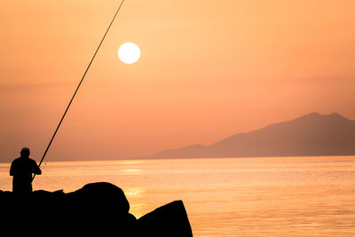 Silhouette man fishing by sea against sky during sunset