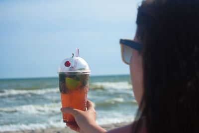 Close-up of woman holding drink at beach against sky