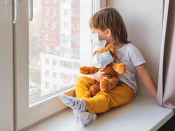 Boy with teddy bear on window
