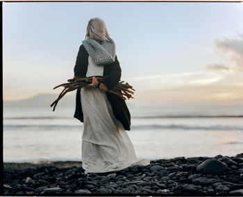 Rear view of woman holding umbrella on beach against sky