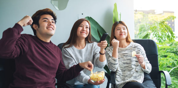 Friends eating potato chips while cheering and watching game on tv together