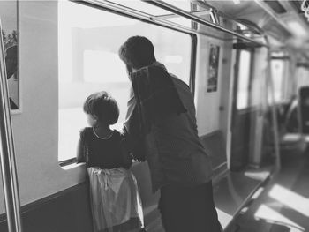 Rear view of man and girl looking through window in train