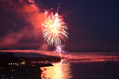 Firework display over sea against sky at night