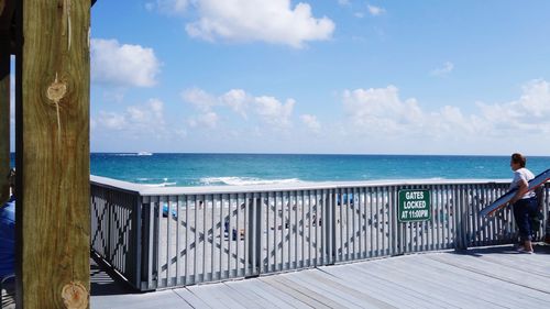 Woman standing at pier by sea against sky