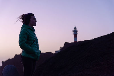 Side view of woman standing by lighthouse against sky