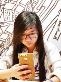 Young woman using smart phone while sitting against wall in cafe