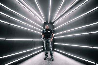 Full length portrait of young man standing against illuminated wall