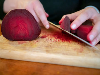 Cropped hands of person cutting common beet in kitchen