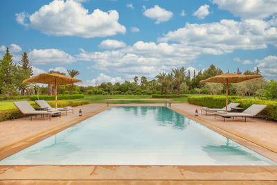 Swimming pool view with blue cloudy sky and deckchairs to relax