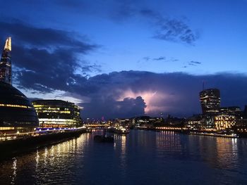 Illuminated city by river against sky at night