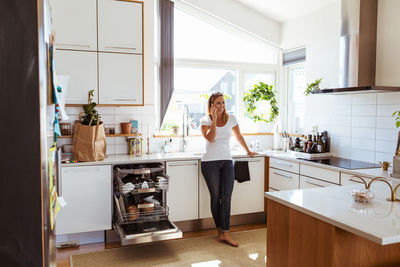 Smiling woman talking on mobile phone while standing in kitchen