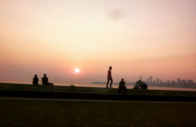 Silhouette people standing on shore against sky during sunset