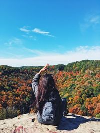 Rear view of woman sitting on autumn leaves against sky