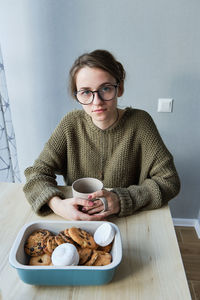 Millennial brown-haired girl drinks tea with cakes alone