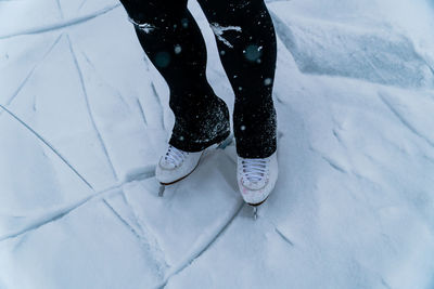 Lower section of a person with ice skates on a snowy frozen pond.