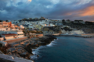 View of city at waterfront against cloudy sky