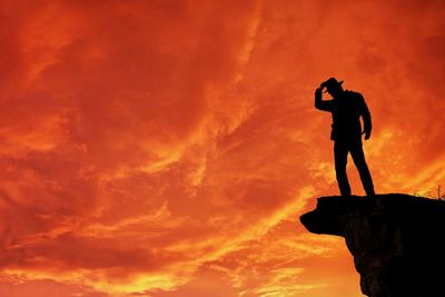 Low angle view of silhouette man standing against orange sky