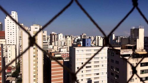 Cityscape seen through chainlink fence against sky