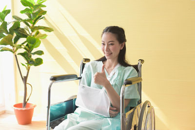 Smiling disabled woman gesturing while sitting on wheelchair against wall