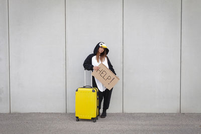 Full length of woman holding yellow while standing against wall