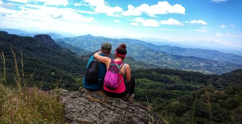 Rear view of couple sitting on rock against sky