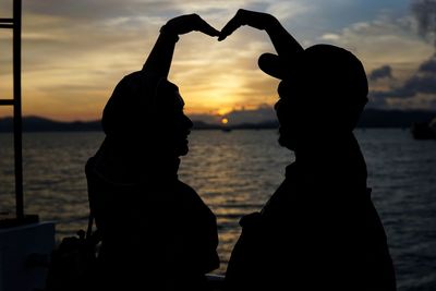 Silhouette couple standing by sea against sky during sunset