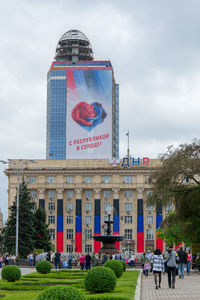 Group of people in front of building against cloudy sky