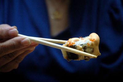 Midsection of woman holding sushi with chopsticks