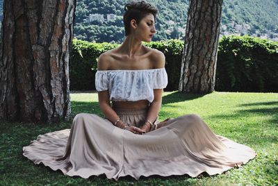 Young woman relaxing on grassy field against trees