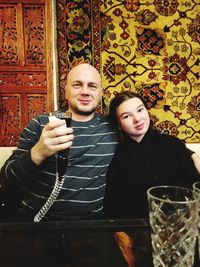 Portrait of young woman with man holding wineglass while sitting at restaurant