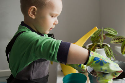 Four-year-old boy in an apron and gloves pours the ground into a pot of plants