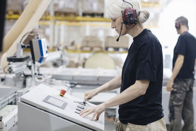 Side view of female worker wearing ear protectors operating machine at industry