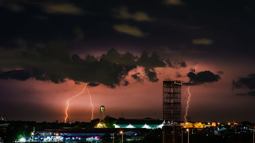 Scenic view of illuminated city against sky at night with massive lightning strikes