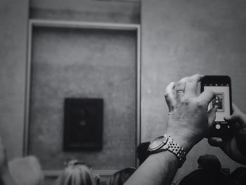 Cropped hand photographing mona lisa painting at museum