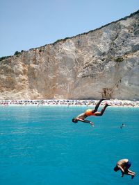 People on rocks by sea against clear blue sky