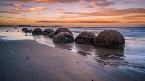 Rocks on beach against sky during sunset