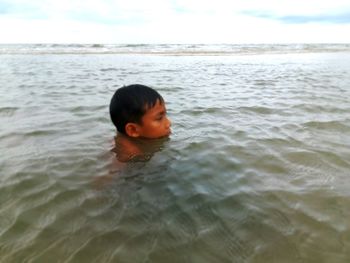 Boy swimming in sea against sky