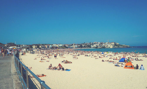 People at beach against clear blue sky