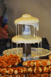 Close-up of white chocolate fountain by waffles at table
