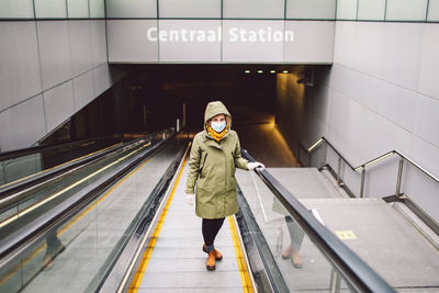 Portrait of woman wearing mask standing on escalator at subway station