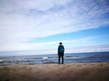 Rear view of woman standing at beach against sky