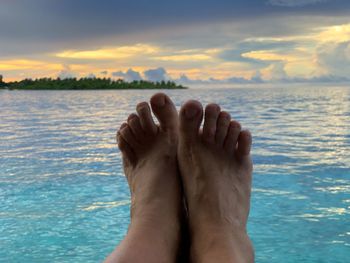 Low section of woman in sea against sky during sunset