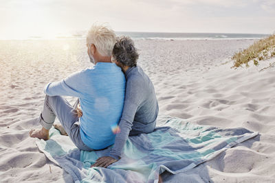 Back view of couple sitting on the beach looking to the sea