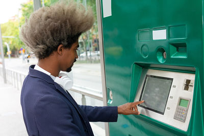 Side view of african young man with afro hair pulling out a ticket on the tram wearing a wireless headset around his neck