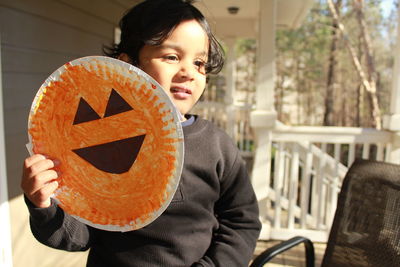 Girl holding pumpkin mask at porch