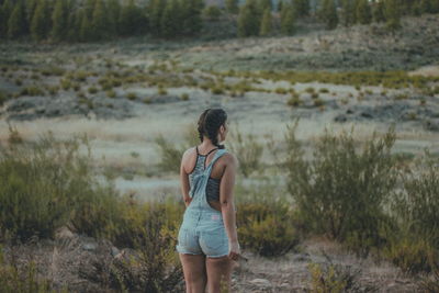 Rear view of young woman walking on landscape against sky